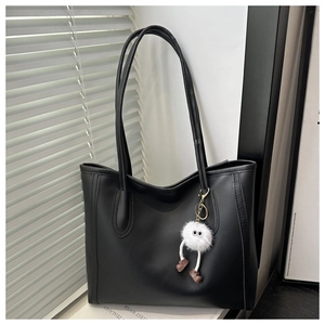 Detail of black leather tote bag featuring a fluffy monster keychain and soft leather texture