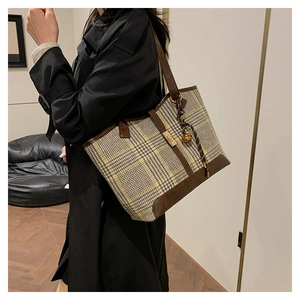 Detail view of a plaid wool tote bag with brown leather trim and golden buckle