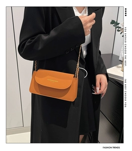 Détail du petit sac orange vif à rabat avec bandoulière chaîne dorée sur blazer