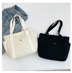 Detail of minimalist canvas tote bags in black and white with side pockets and metal snap