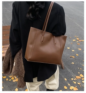Detail of a dark brown matte leather tote bag worn on shoulder in autumn street style setting