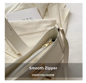 Close-up of smooth gold zipper and stitching detail on a cream white leather shoulder bag