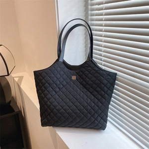 Detail of black quilted tote bag featuring a gold clover logo and leather handles
