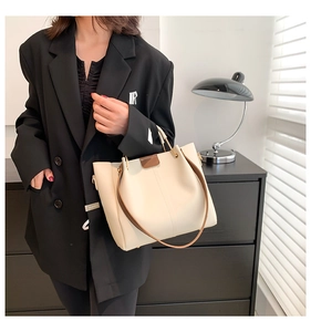 Close-up of beige leather tote bag featuring brown contrast straps and metallic buckles