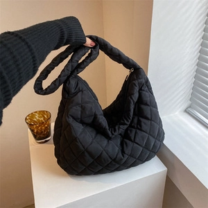 Detail of black quilted puffer tote bag with diamond stitching on a white pedestal