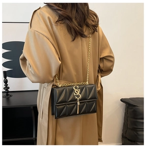 Detail of a black quilted crossbody bag with gold S-buckle, fringe, and chain strap