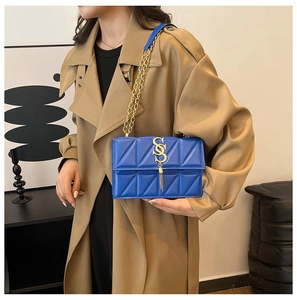 Detail of blue quilted square bag with gold SS logo and elegant metal fringe