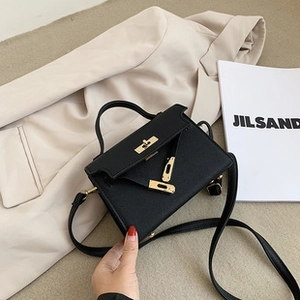 Close-up of black textured leather mini tote bag with gold hardware on a beige blazer