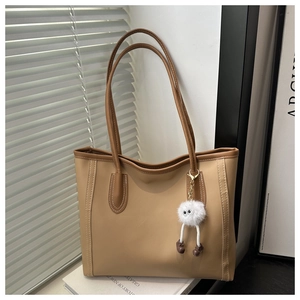 Detail of khaki leather tote bag with dark brown stitching and cute white monster charm