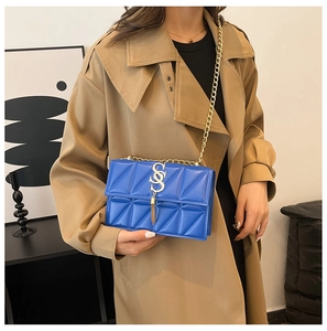 Detail of royal blue quilted chain bag with gold S-hardware and fringe on a trench coat