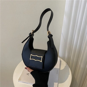 Detail of minimalist black hobo shoulder bag with a rectangular gold buckle on a white table