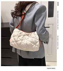 Detail of beige quilted puffer tote bag with orange strap and fashion bag label