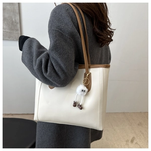 Minimalist cream tote bag with brown trim and plush monster charm on a model's shoulder