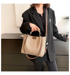 Business style beige PU leather tote bag with brown handles worn by a model in a suit