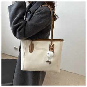 Detail of minimalist cream tote bag with brown trim and plush charm worn by model