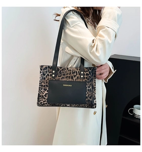 Detailed view of leopard print tote bag featuring black leather front pocket with text