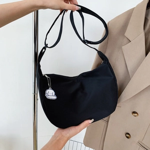 Detail of a black crescent hobo bag featuring a white cartoon cloud pendant and shoulder strap