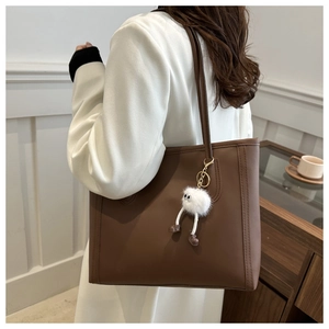 Brown leather tote bag with monster charm detail worn by a model in a minimal setting