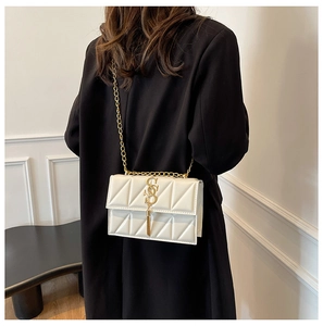 Close-up of white geometric quilted crossbody bag with gold chain and tassel hardware
