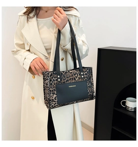 Leopard print tote bag with black strap and front pocket detail held by model