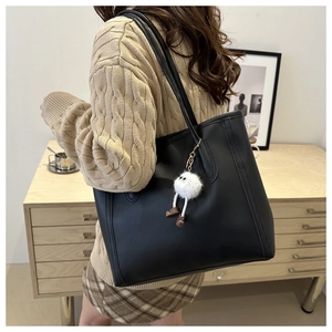 Detail of a black leather tote bag with a white cartoon plush charm on a woman's shoulder