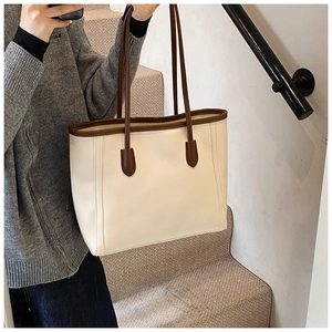 Lifestyle view of a large cream tote bag with brown trim on a woman's shoulder