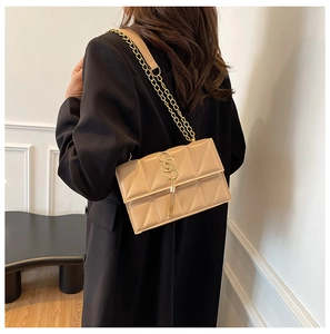 Detail view of a quilted beige shoulder bag with gold chain strap and tassel pendant on a model
