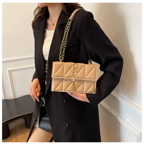 Detail of a beige quilted crossbody bag with gold S-logo and tassel on a black blazer