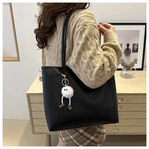 Detail of a black leather tote bag with a plush monster charm on a female model