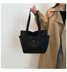 Detail of black canvas tote bag featuring front pocket with gold snap and side storage