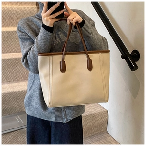 Minimalist cream tote bag with dark brown straps held by a model in a stairwell