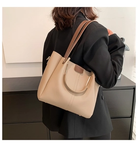 Detail of a beige leather tote bag with brown straps and gold metal ring accent