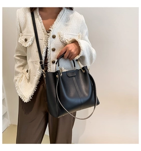 Close-up of black leather bucket tote with gold metal handles on a white tweed jacket