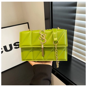 Macro detail of vibrant green quilted handbag with golden S-metal buckle and tassel chain