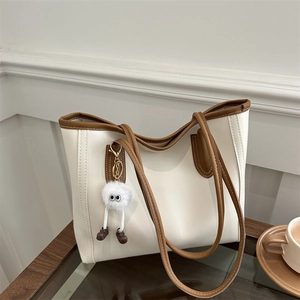 Minimalist vintage cream tote bag with brown trim and plush charm on a wooden desk