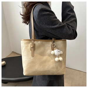 Detail of beige large tote bag with brand logo and white plush doll pendant