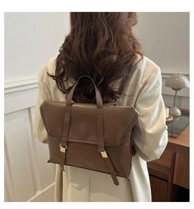 Brown leather backpack with gold buckle closure shown on shoulder in office setting