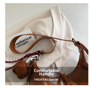Détail d'un sac hobo en cuir marron avec un ourson en peluche sur un blazer ivoire