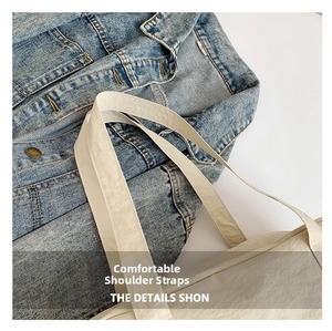 Close-up of beige nylon tote bag with wide shoulder strap against blue denim jacket
