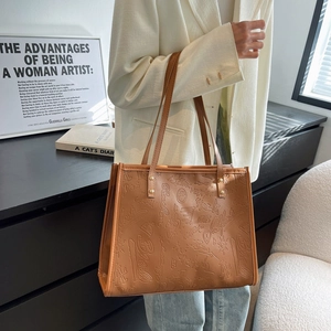 Brown leather tote bag with vintage embossed graffiti patterns and top handles