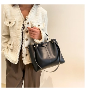 Detailed view of a black faux leather tote bag with gold hardware on a stylish model