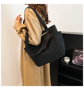 Detail of a large black canvas tote bag with side pocket and sturdy shoulder straps