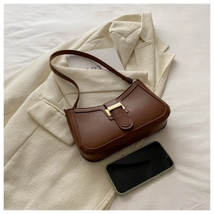 Close-up of brown vintage shoulder bag with gold clasp on a beige blazer and book