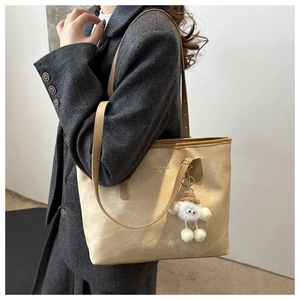Detail of camel suede tote bag with minimalist logo and white plush charm accessory