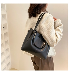 Side view of a vintage black tote bag with gold ring handles on a model in a minimalist setting