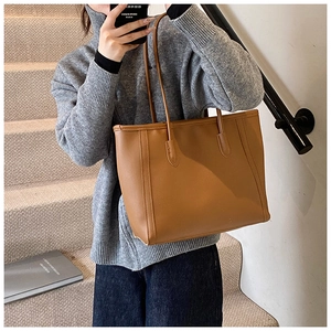 Chic caramel brown tote bag worn on shoulder by model against a minimalist staircase