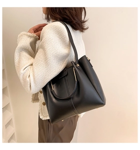 Detail showing high-capacity black matte leather tote bag with curved gold metal handle