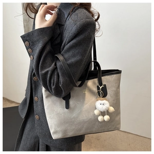 Detail of grey tote bag with gold lettering, black leather straps and plush mascot