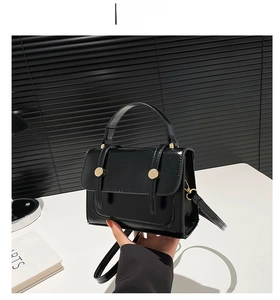 Detail view of the black patent leather crossbody bag with shiny finish and gold buckles