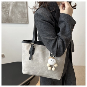 Light gray tote bag with black trim and plush charm shown on a charcoal suit